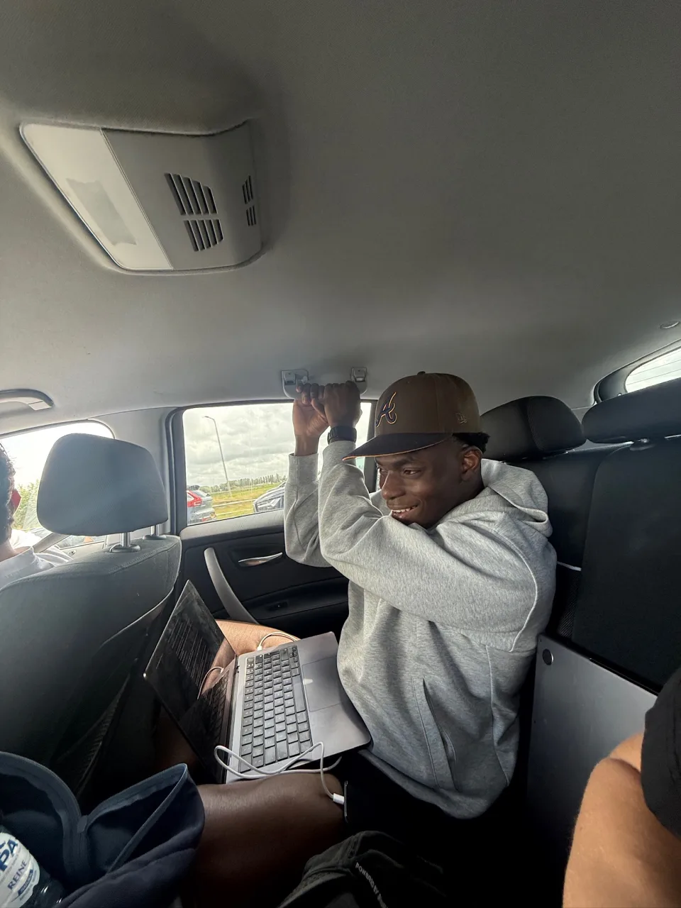 Fathin smiling in the back seat of a car with a laptop open