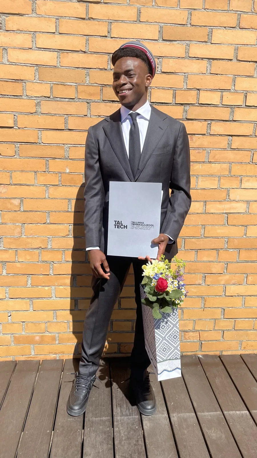 Fathin in a suit holding his TalTech diploma and flowers